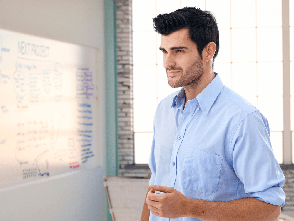 man standing in front of a white board thinking about his business