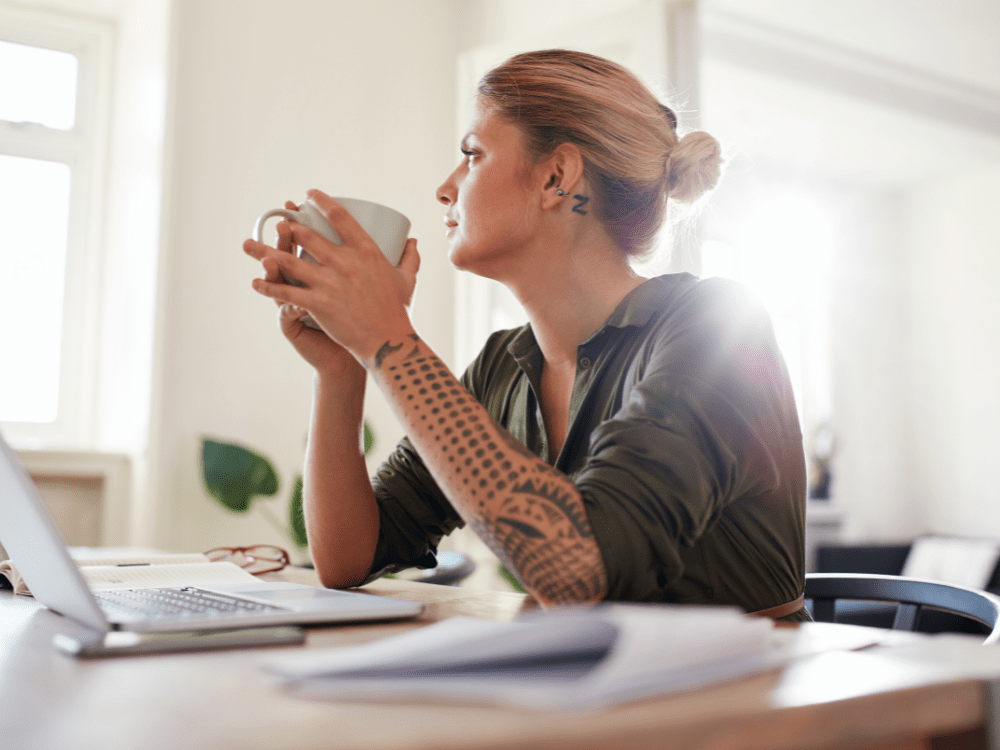 woman holding cup of coffee, thinking in front of her computer